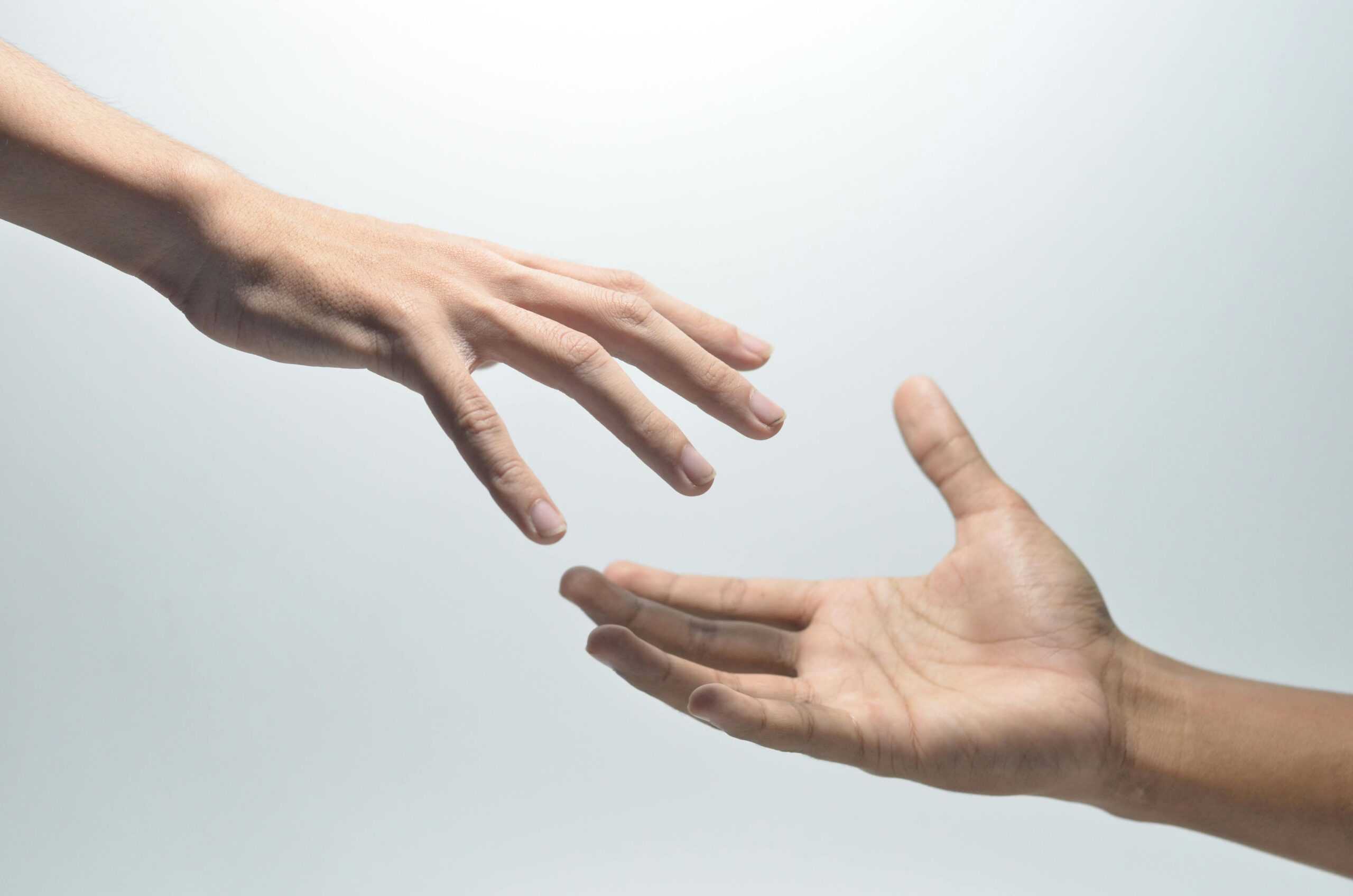 Close-up of two hands reaching towards each other on a neutral background, symbolizing connection.
